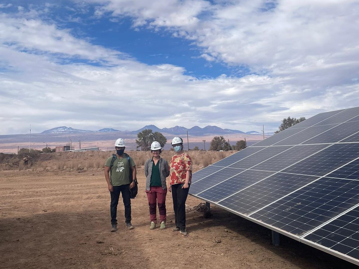 Group photo of three persons standing next to solar panels in the Atacama desert