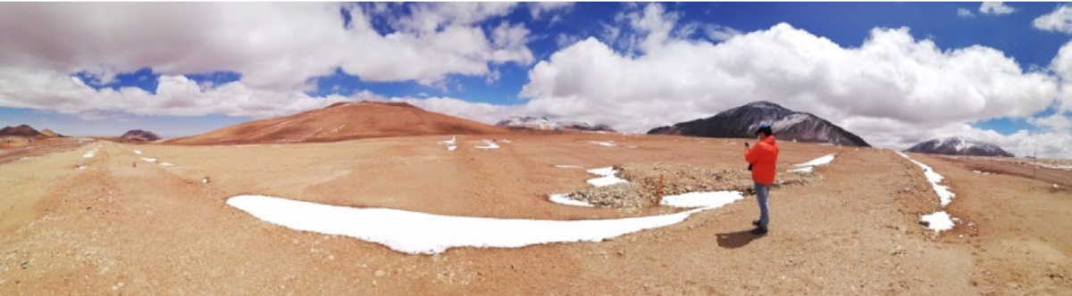 panoramic picture of a chilean desert with orange soil, blue sky with white clouds and some snow