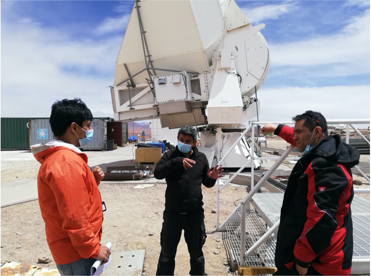 photo of three persons discussing in front of a telescope in the desert